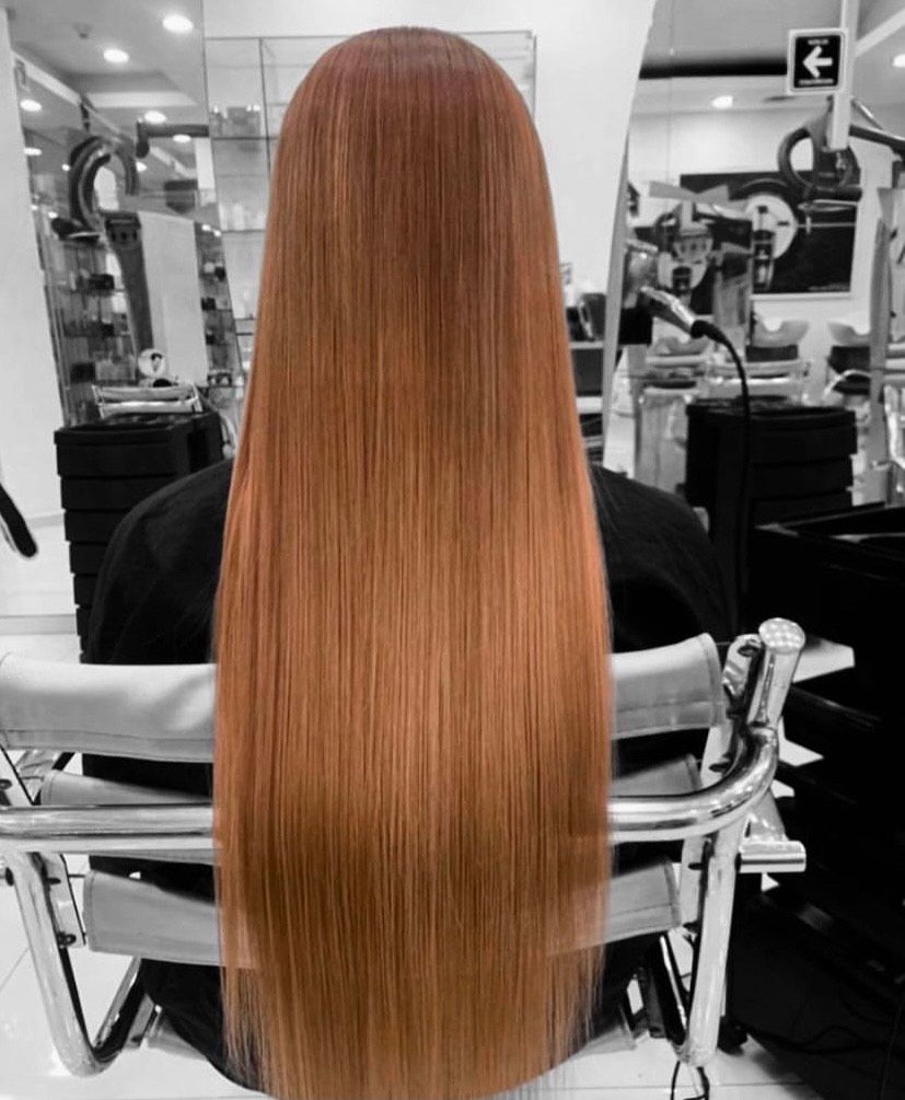 Persona con cabello largo, liso y cobrizo, sentada en una silla de peluquería, vista desde atrás.