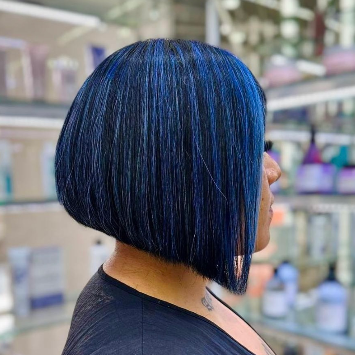 Perfil de una persona con un elegante corte de pelo bob azul en el pasillo de una tienda.