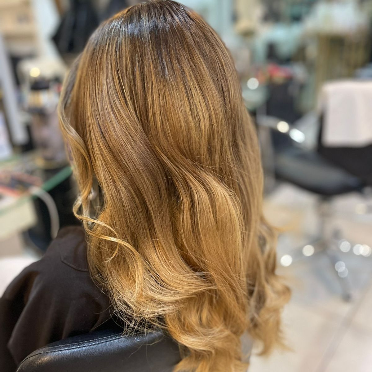 Cabello ondulado rubio-castaño hasta los hombros, peinado en una silla de peluquería.