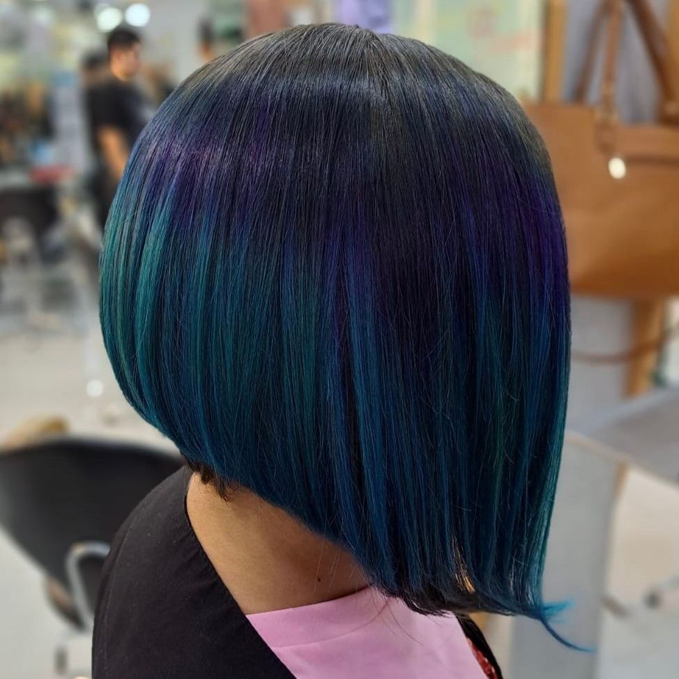 Corte de pelo bob corto con reflejos azul oscuro y verde azulado, visto de perfil en una peluquería.