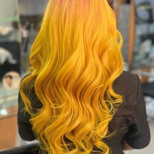 Vista trasera de una larga melena ondulada de color amarillo anaranjado brillante sobre una blusa negra.