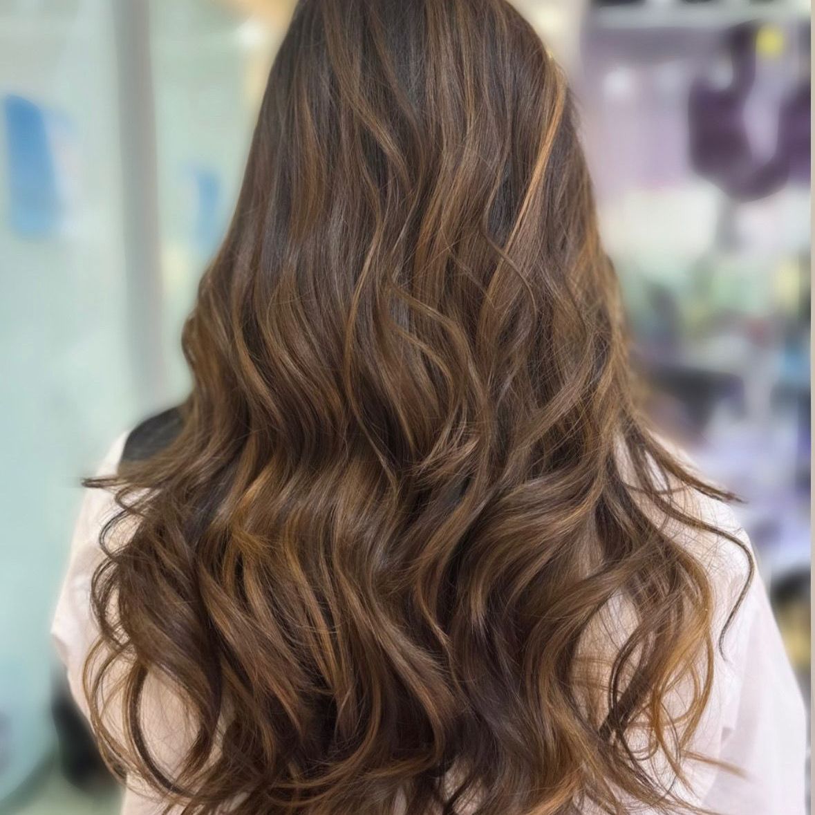 Cabello castaño largo y ondulado visto desde atrás en un entorno interior suavemente desenfocado.