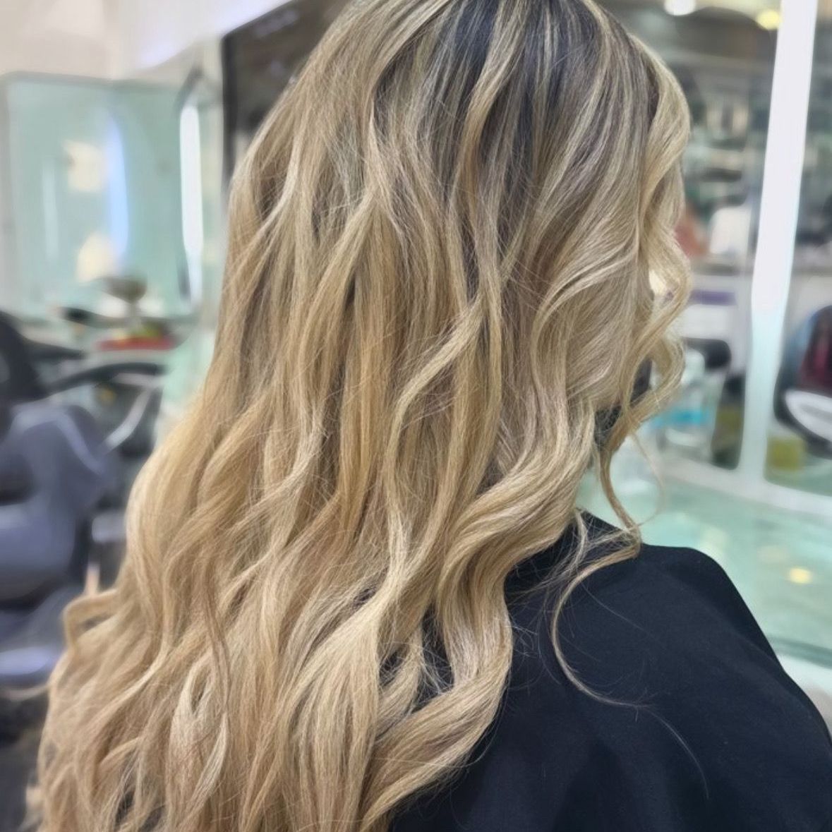 Cabello rubio ondulado con reflejos, visto desde atrás en un salón de belleza.
