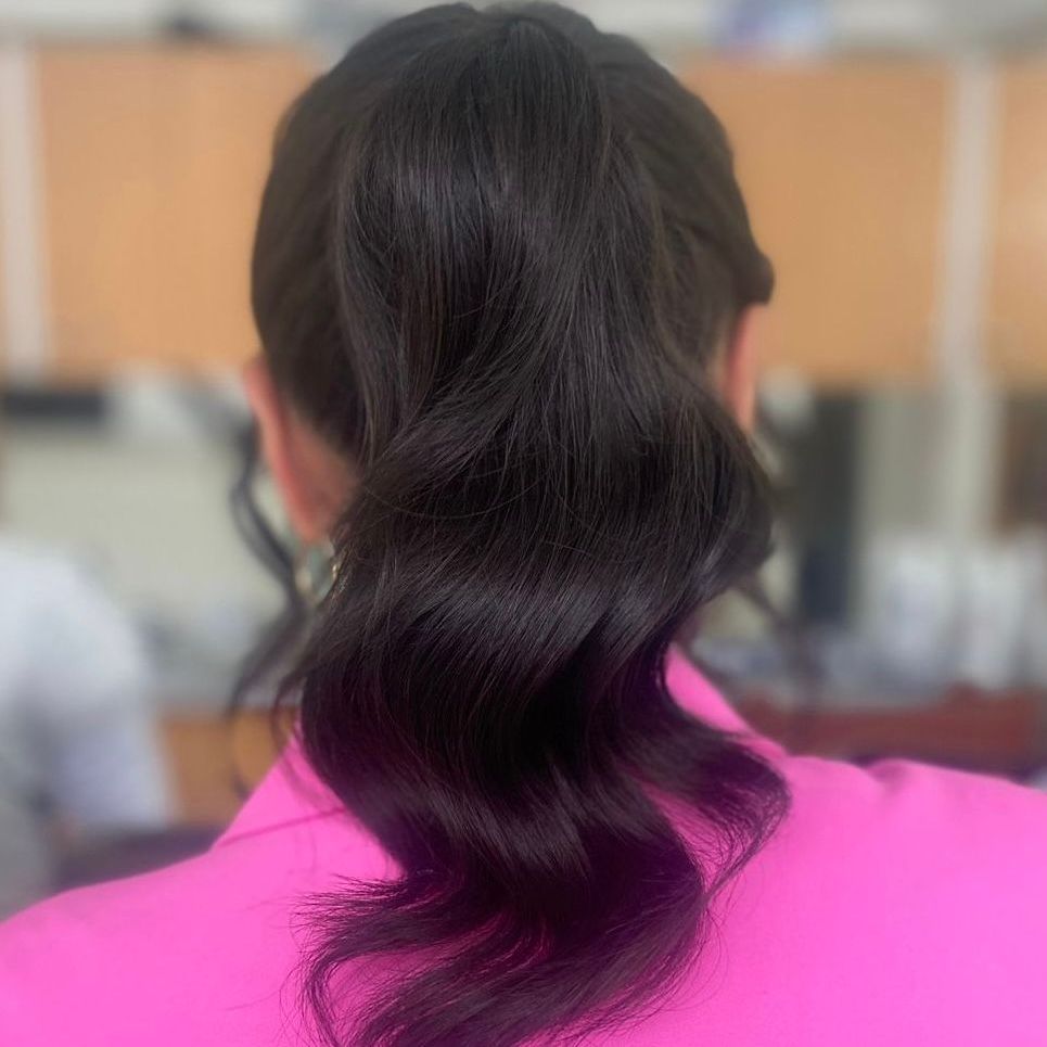 Vista trasera de una melena oscura y ondulada recogida en una coleta baja con una blusa de color rosa brillante.