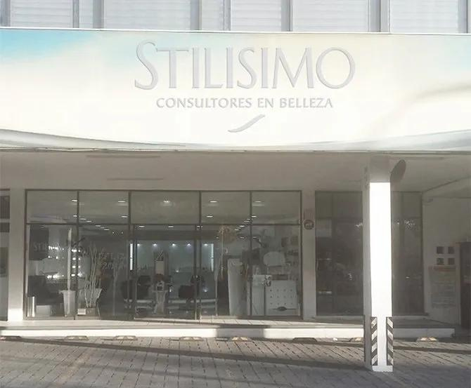 Fachada de “STILISIMO Consultores en Belleza” con entrada de cristal y fachada blanca.