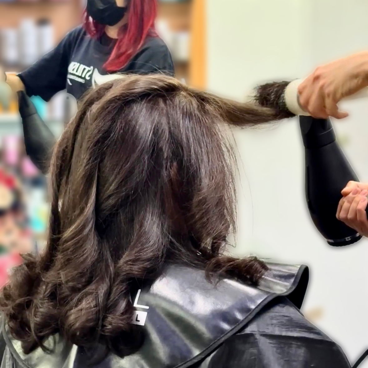 Peluquera secando con secador el cabello oscuro de una mujer en un salón de belleza.