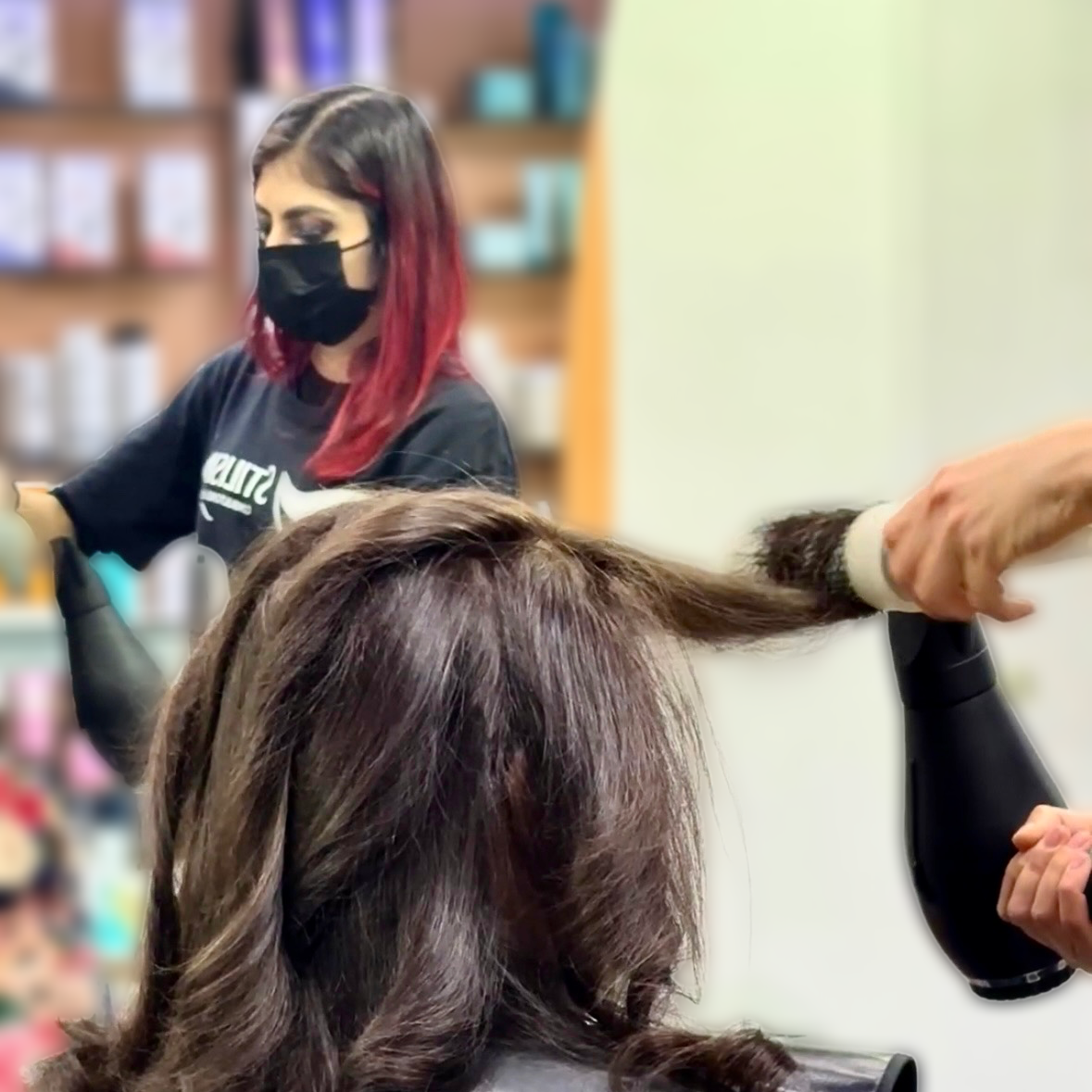 Una estilista seca con secador el cabello castaño de una clienta en un salón de belleza.
