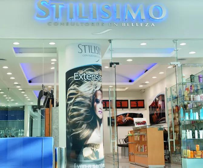 Entrada del salón Stillissimo con letrero azul, puertas de cristal y un póster de una mujer con el pelo peinado.