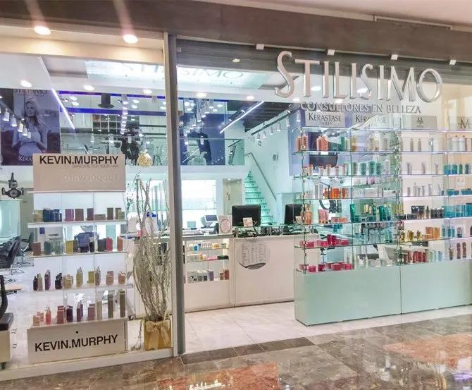 Fachada de salón de belleza con ventanas de cristal, productos Kevin Murphy y un mostrador blanco.