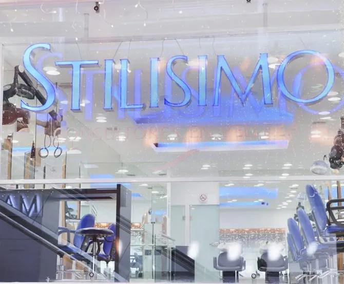 Fachada del salón StylishMO con letrero de neón azul y un interior moderno visible a través del cristal.