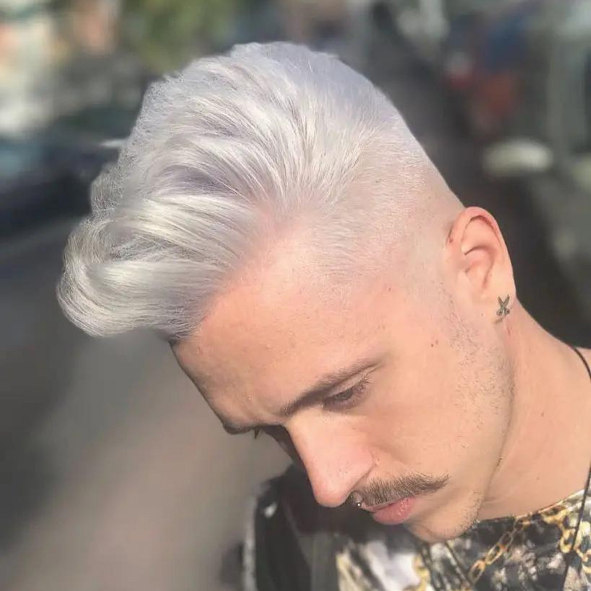Primer plano de un hombre con cabello plateado mirando hacia abajo al aire libre bajo la luz del sol.
