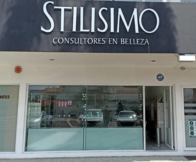 Fachada de “STILISMO Consultores en Belleza” con ventanas de cristal y una fachada blanca.