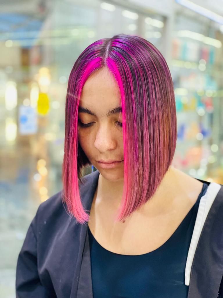 Persona con corte de pelo bob magenta mirando hacia abajo en un entorno interior borroso.