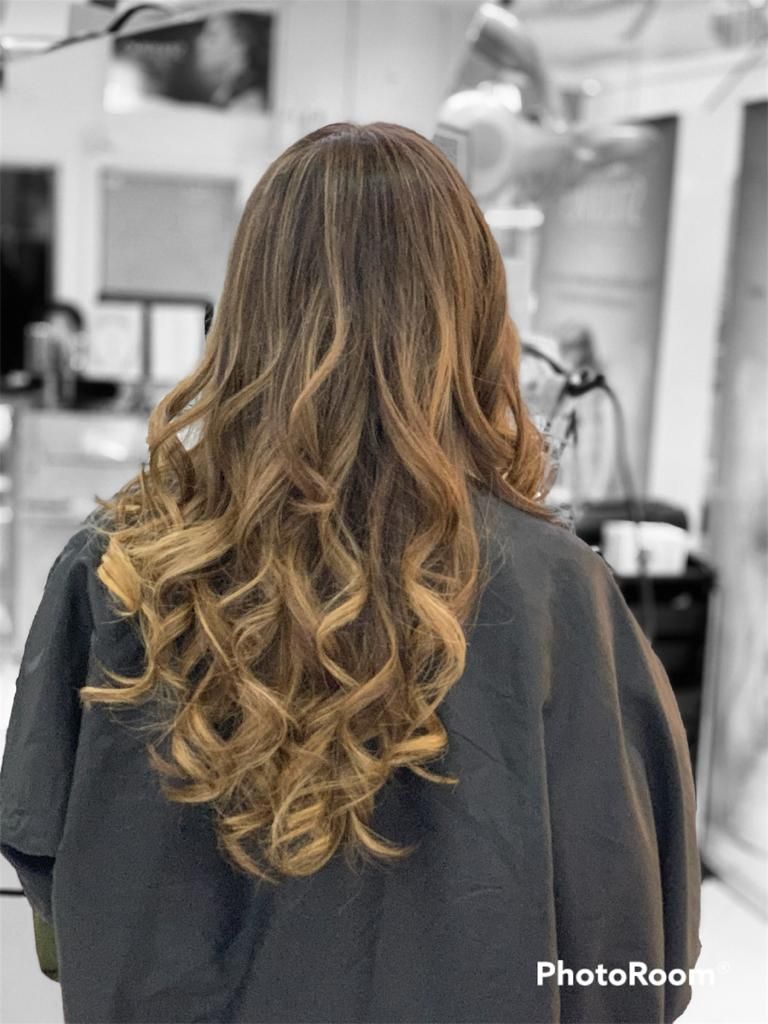 Cabello largo y ondulado castaño con reflejos rubios, visto desde atrás en una silla de peluquería.