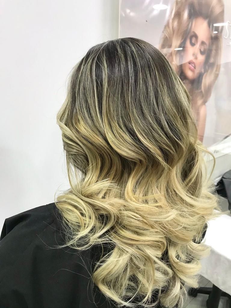 Ondas balayage rubias en cabello hasta los hombros, peinadas en rizos sueltos sobre un fondo de salón.