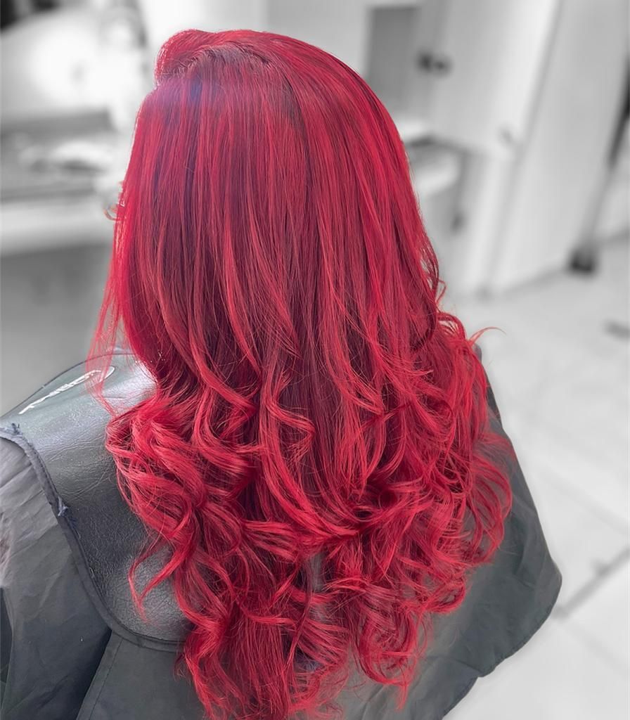 Cabello rizado de color rojo brillante peinado en ondas sueltas sobre una persona que lleva una capa oscura de peluquería.