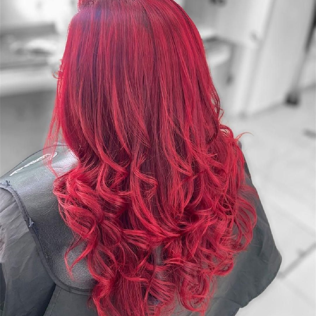 Cabello rizado de color rojo brillante peinado en ondas sueltas sobre un fondo de salón de belleza borroso.