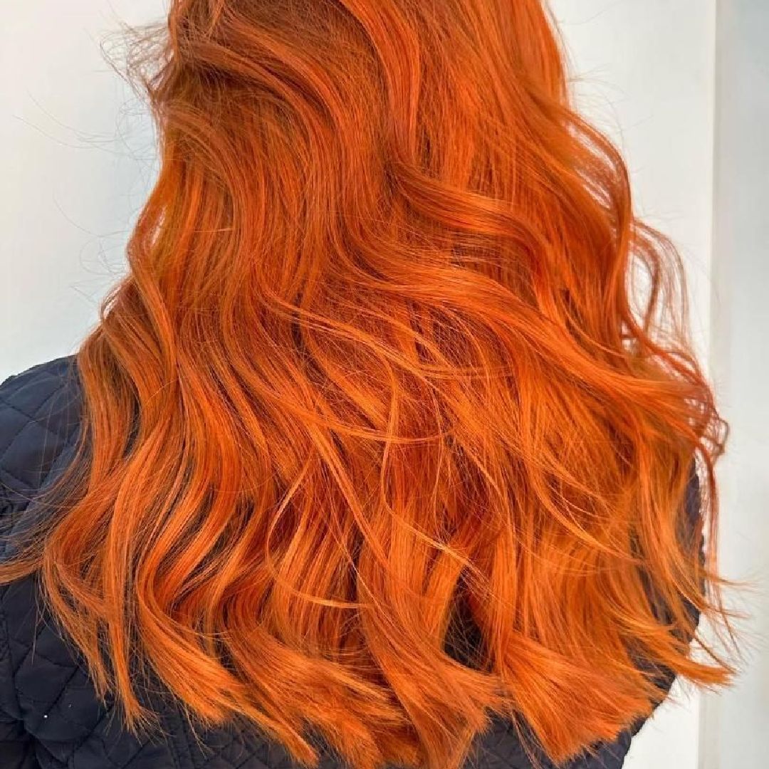 Cabello ondulado de color naranja rojizo vibrante sobre un fondo claro.