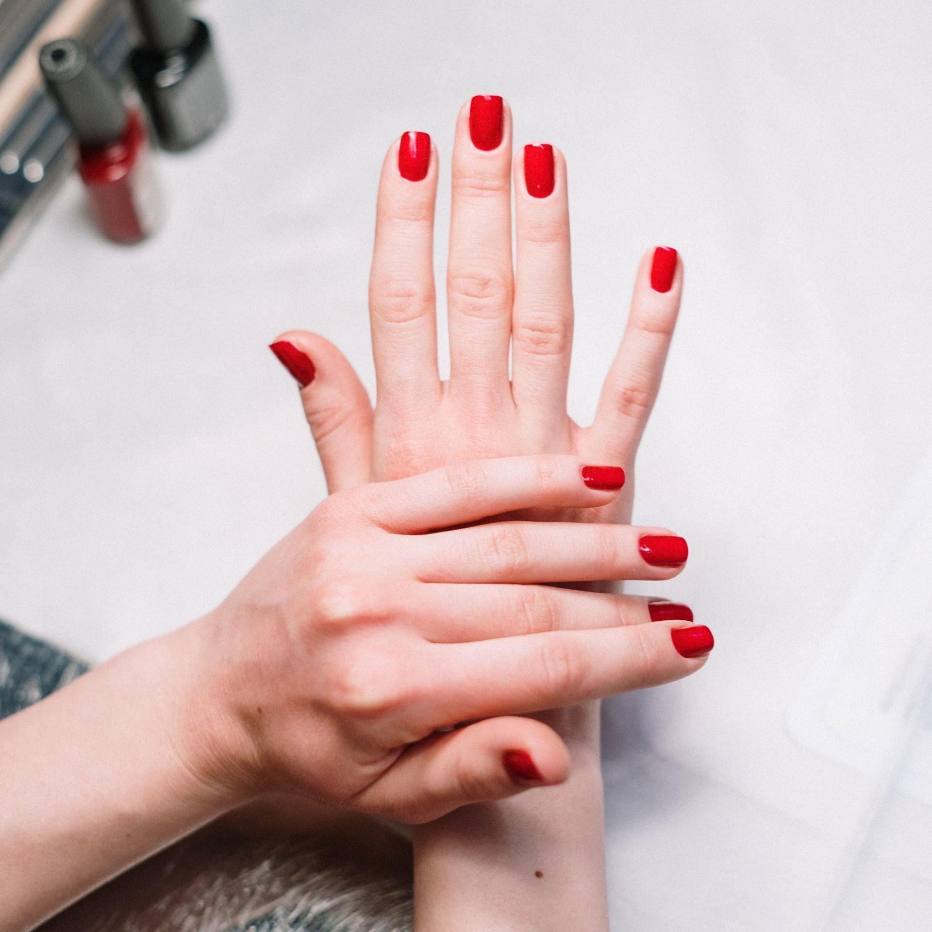 Manos con las uñas pintadas de rojo, suavemente cruzadas sobre un fondo blanco.