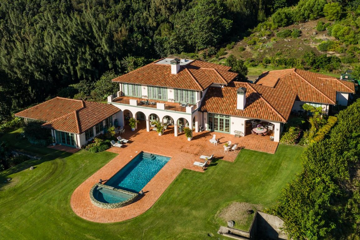 An aerial view of a large house with a swimming pool surrounded by trees.