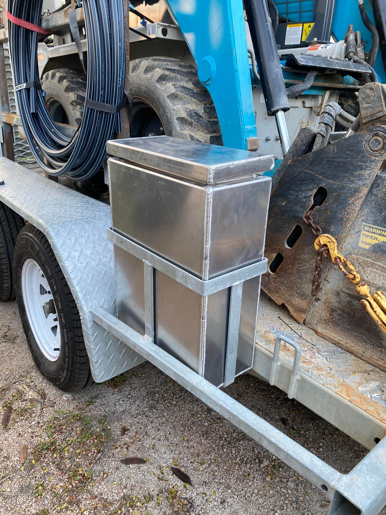 A metal storage box mounted to the frame of a trailer next to a heavy-duty tire and machinery.