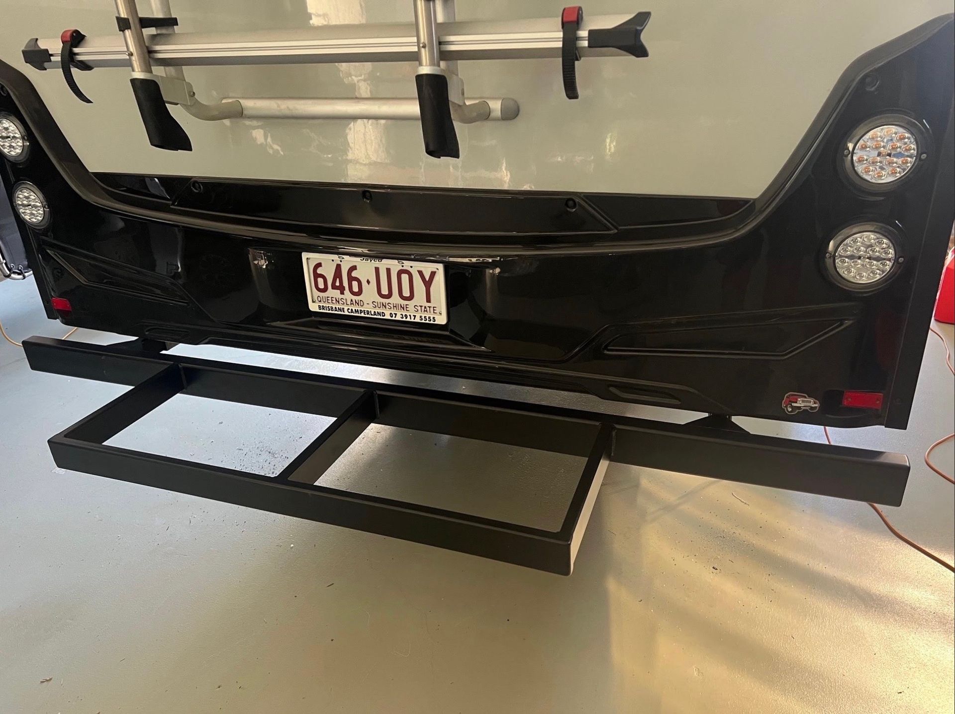 The rear end of a vehicle featuring a Queensland license plate, circular tail lights, and a black metal storage rack.