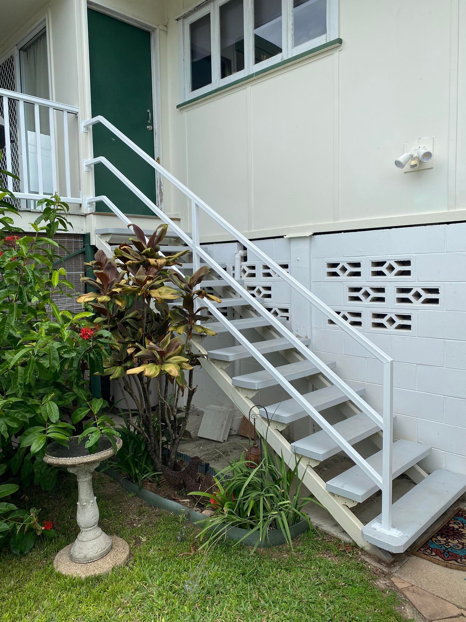 Outdoor staircase with white railings leading up to a green door, positioned next to a white cinder block wall.
