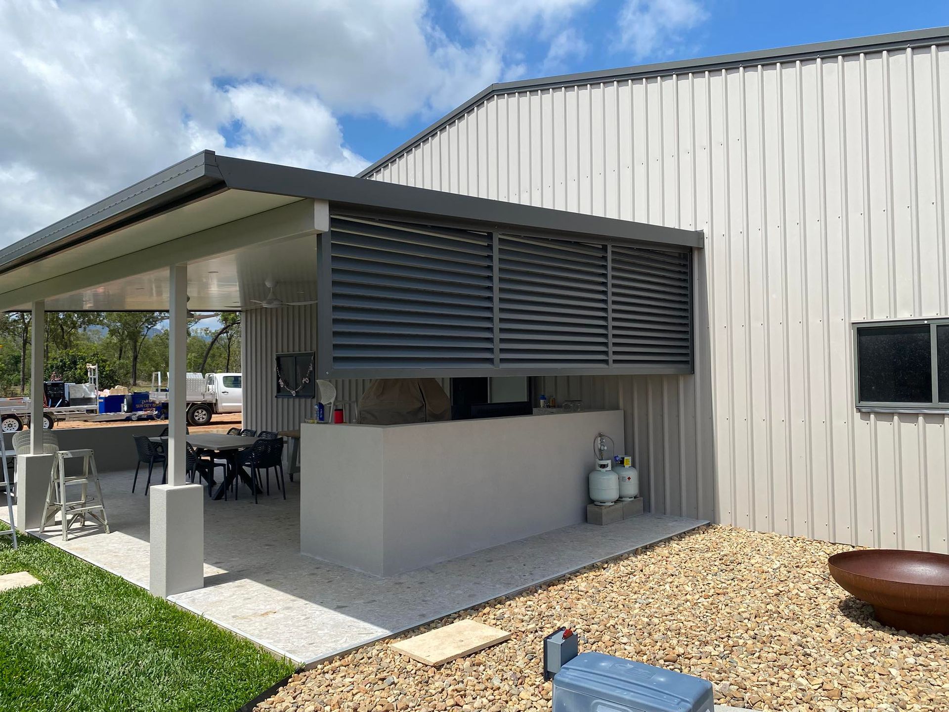 An outdoor kitchen and patio area with a gray slatted privacy screen, concrete counter, and dining table under a roof.
