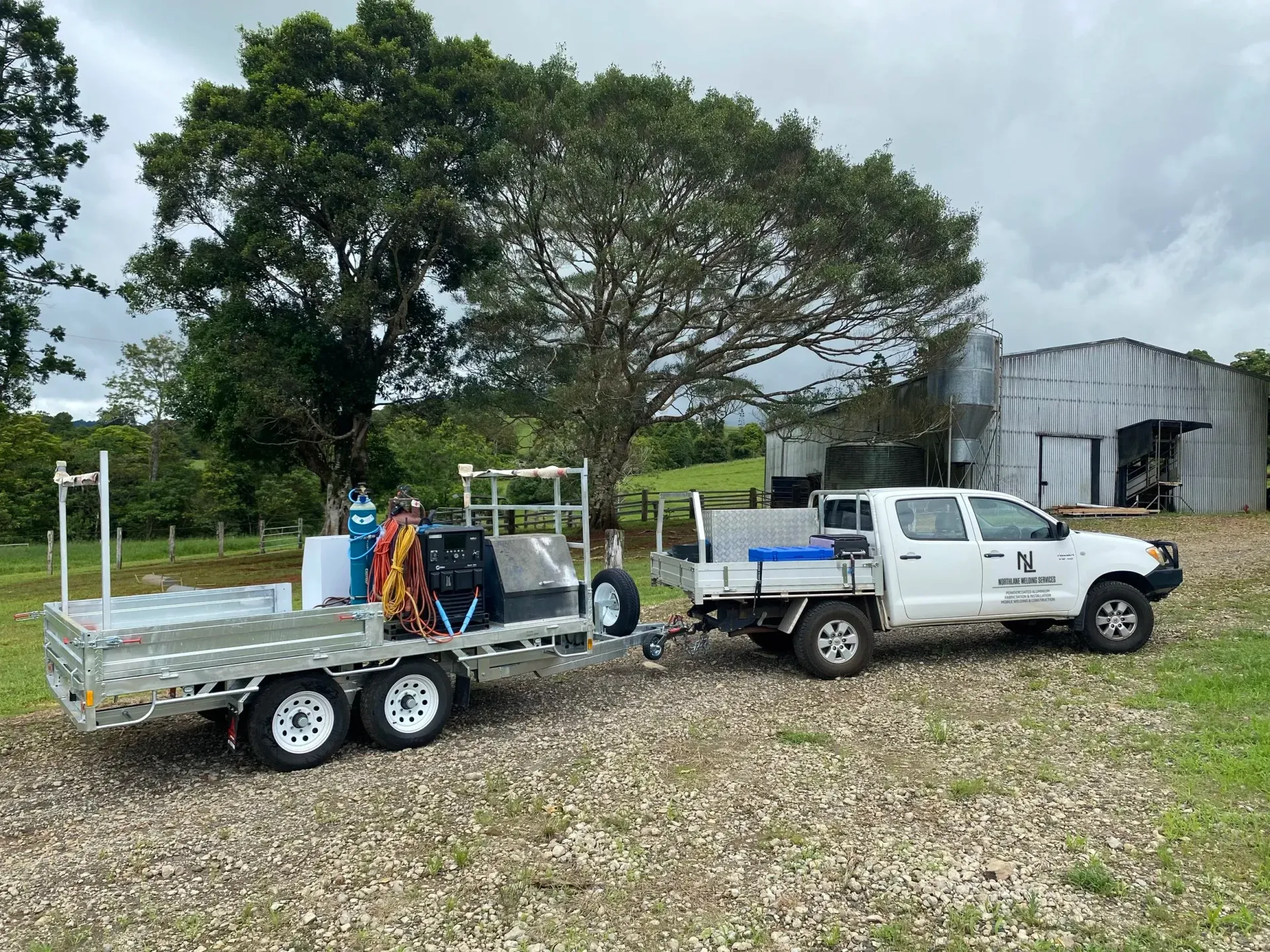 A silver metal toolbox mounted on the side of a trailer next to a heavy-duty piece of machinery.