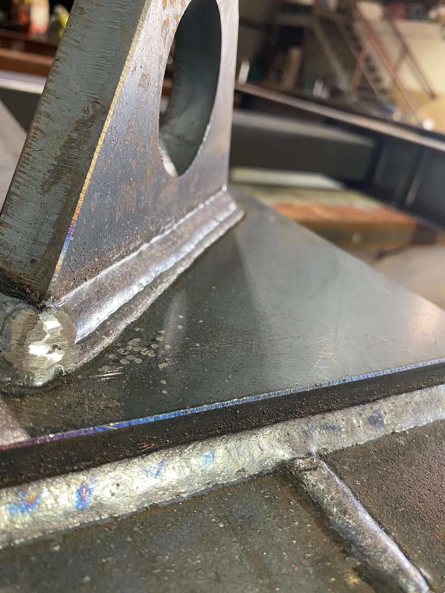 A close-up view of a metal lifting lug welded onto a dark steel plate, showing industrial weld beads.