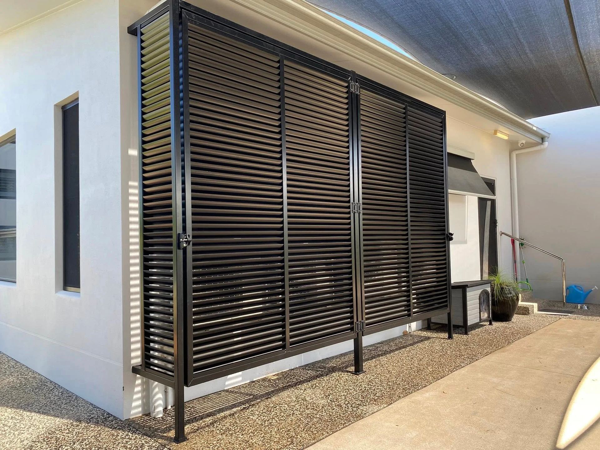 A black metal privacy screen with horizontal louvers installed against the white exterior wall of a house.
