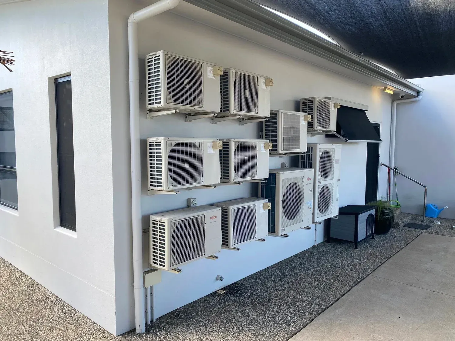 White exterior wall featuring several wall-mounted air conditioning units above a gravel pathway.