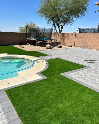 Backyard with pool, artificial turf, and paved patio; trampoline and tree in the background.