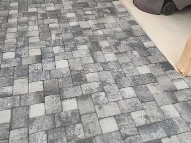 Gray and white rectangular pavers in a herringbone pattern on a patio next to a building.