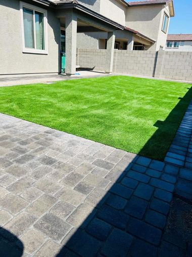 Artificial green lawn surrounded by brick pavers and a light beige house.