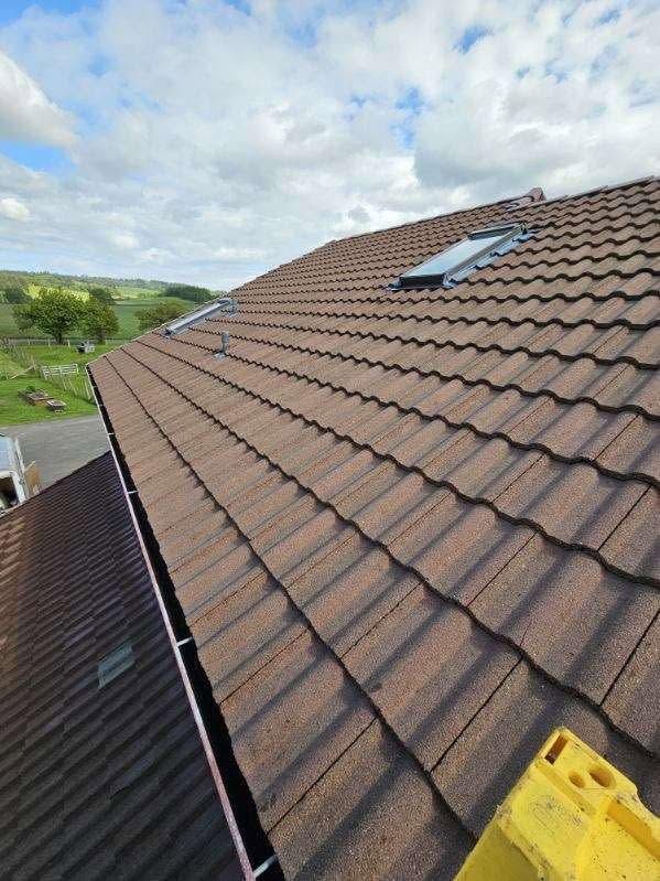 Roof with brown tiles and skylights viewed from a ladder under a cloudy sky