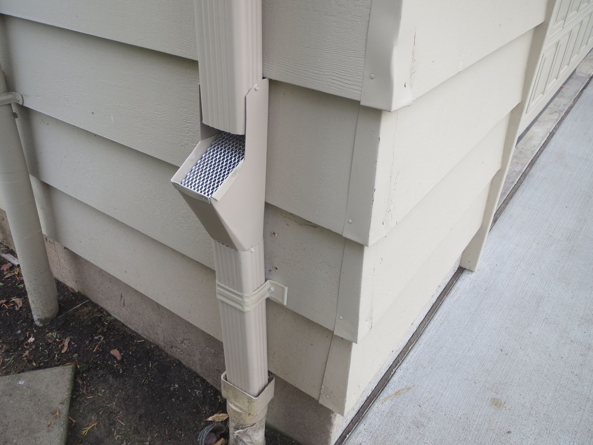 House corner with gray siding and a white downspout running to the ground