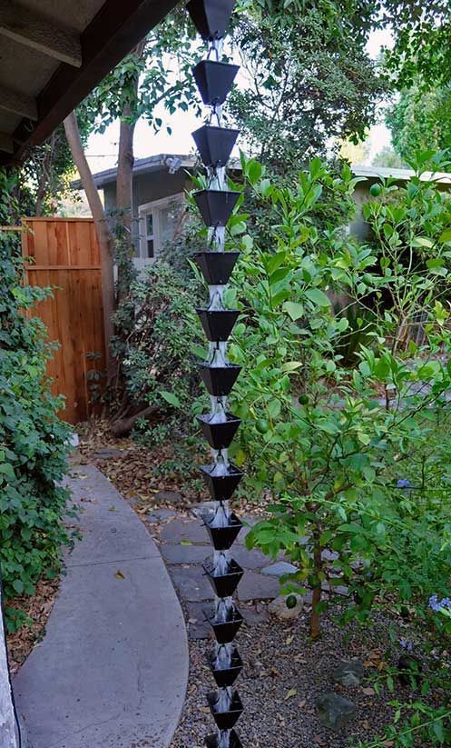 Black-and-white hanging wind chime in a leafy garden beside a curved path and wooden fence