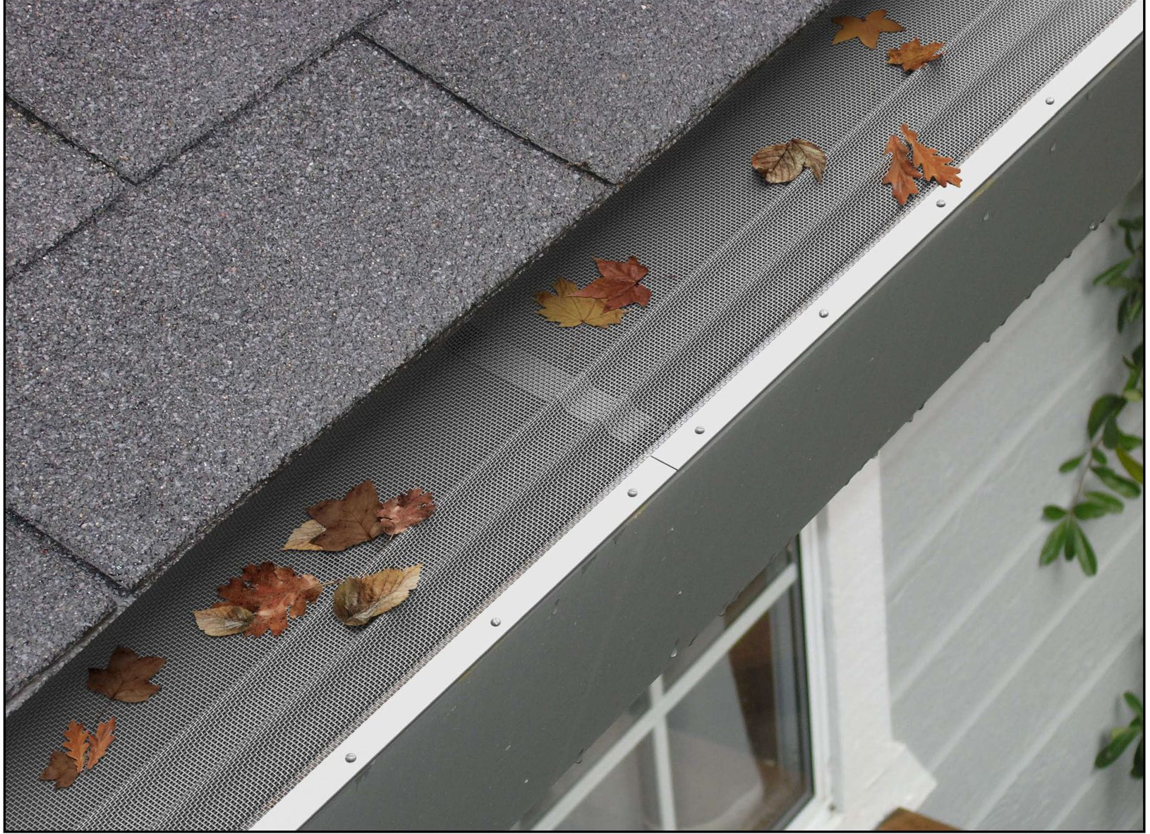 Black perforated gutter guard along a shingled roof edge against a grassy yard.