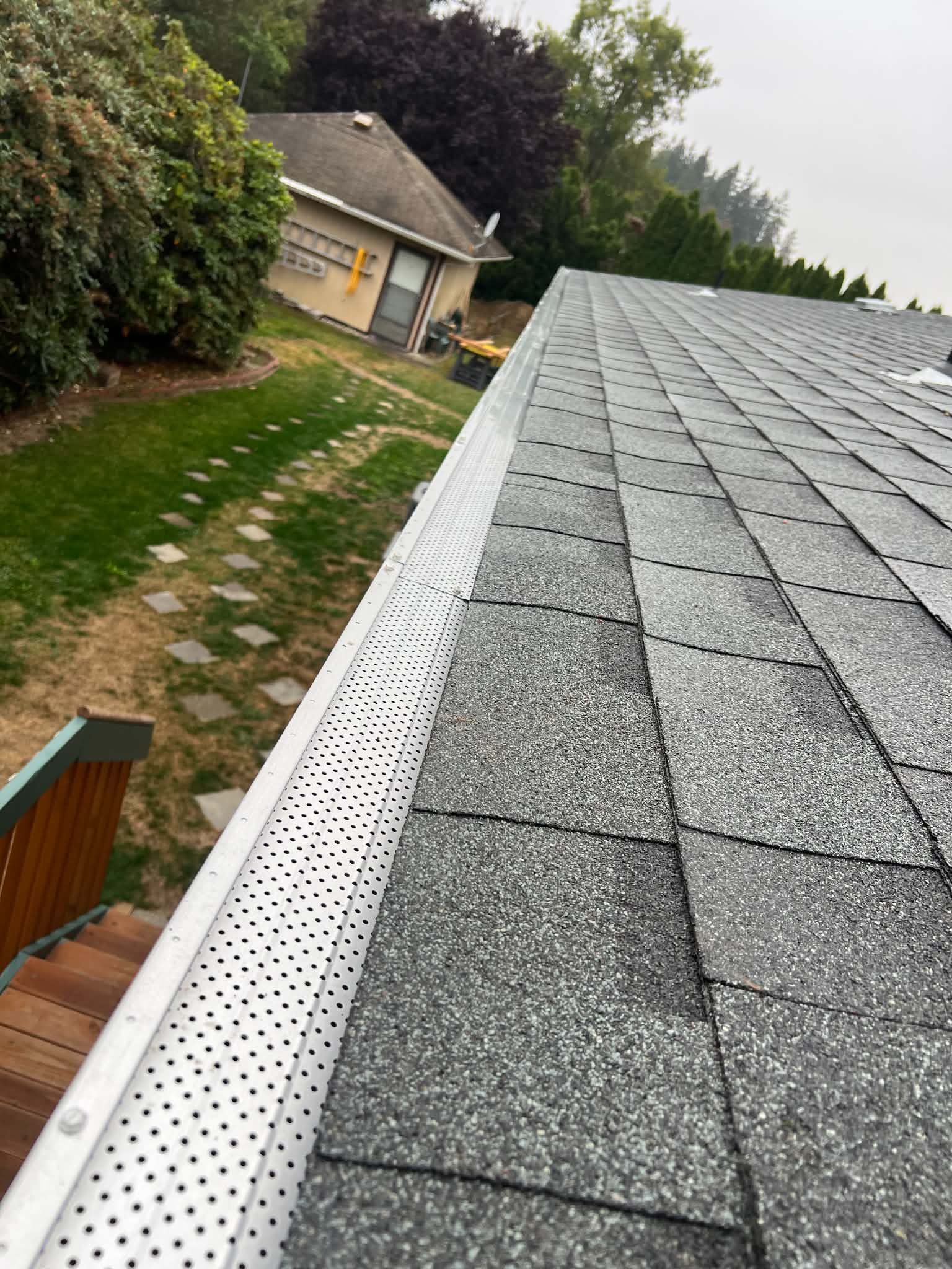 Roof shingles and gutter on a house, viewed from above beside a grassy yard and garden path