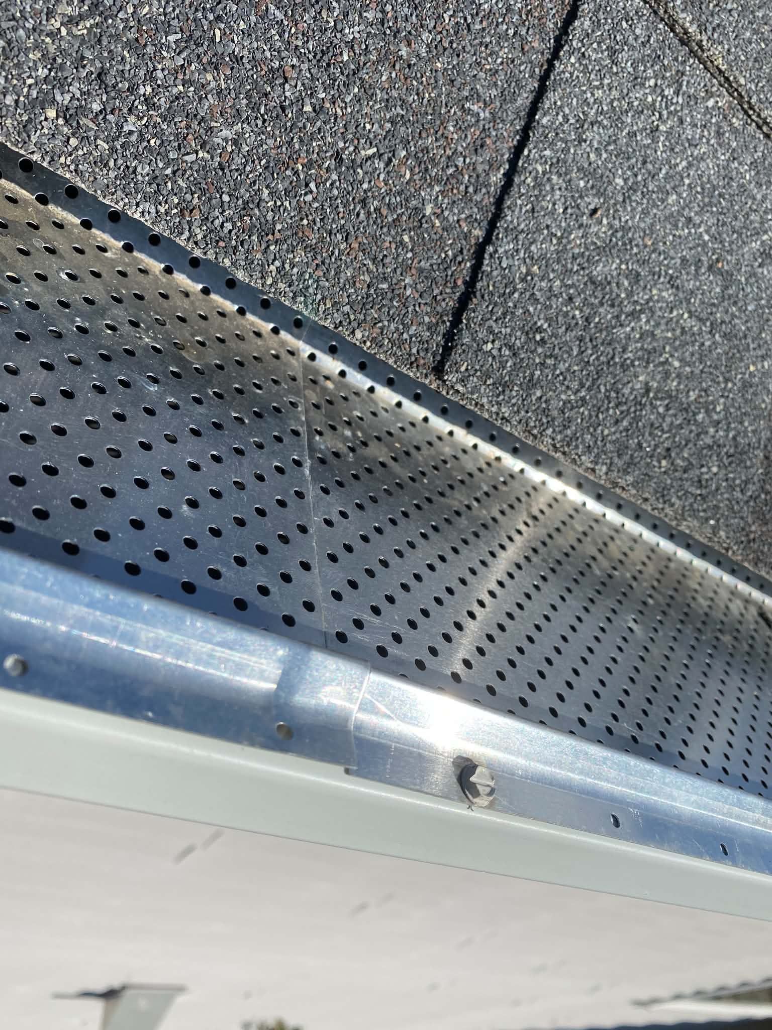 Close-up of a roof edge with gray shingles, perforated metal trim, and white siding.