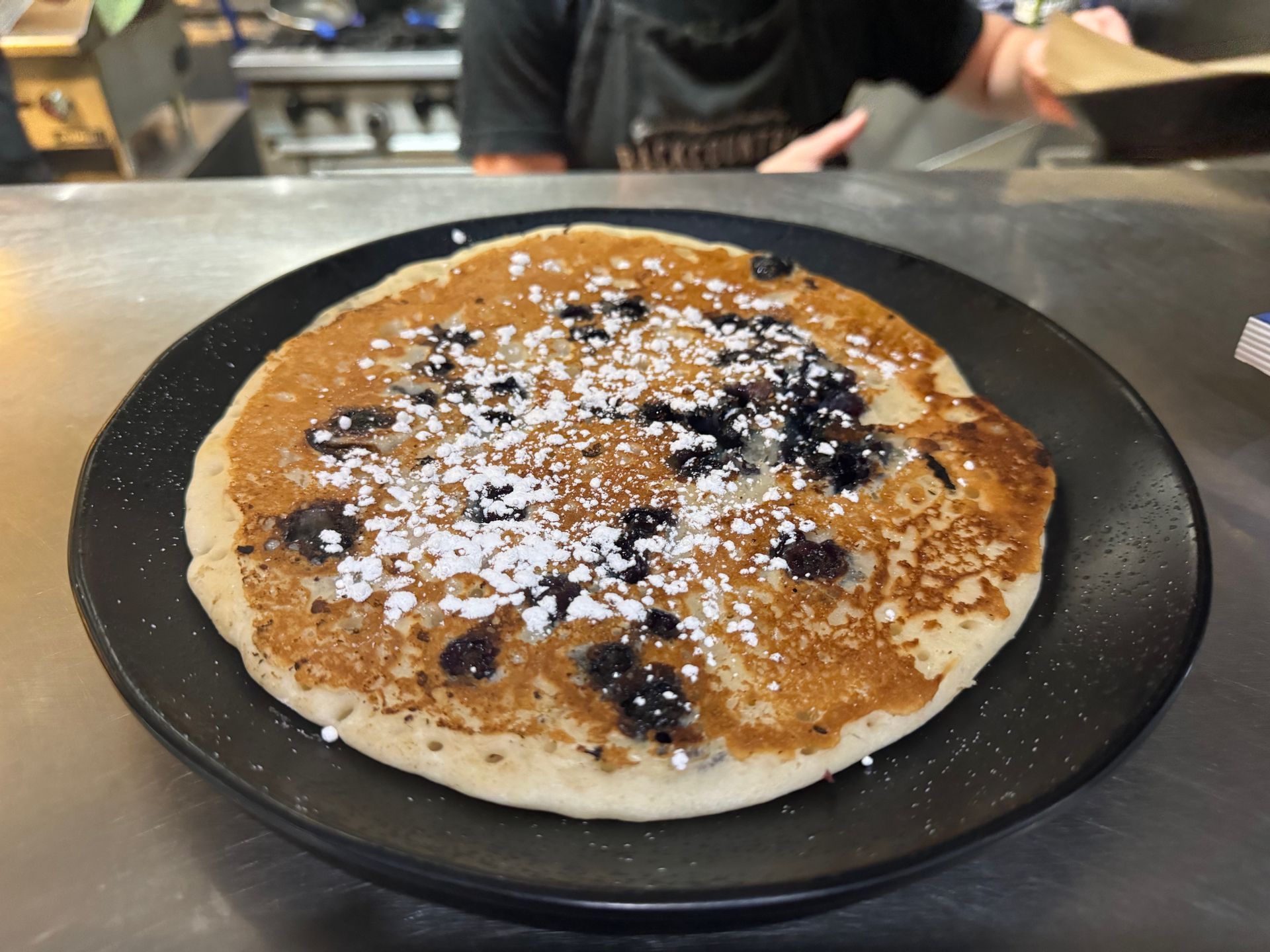 A pancake with blueberries and powdered sugar on a black plate