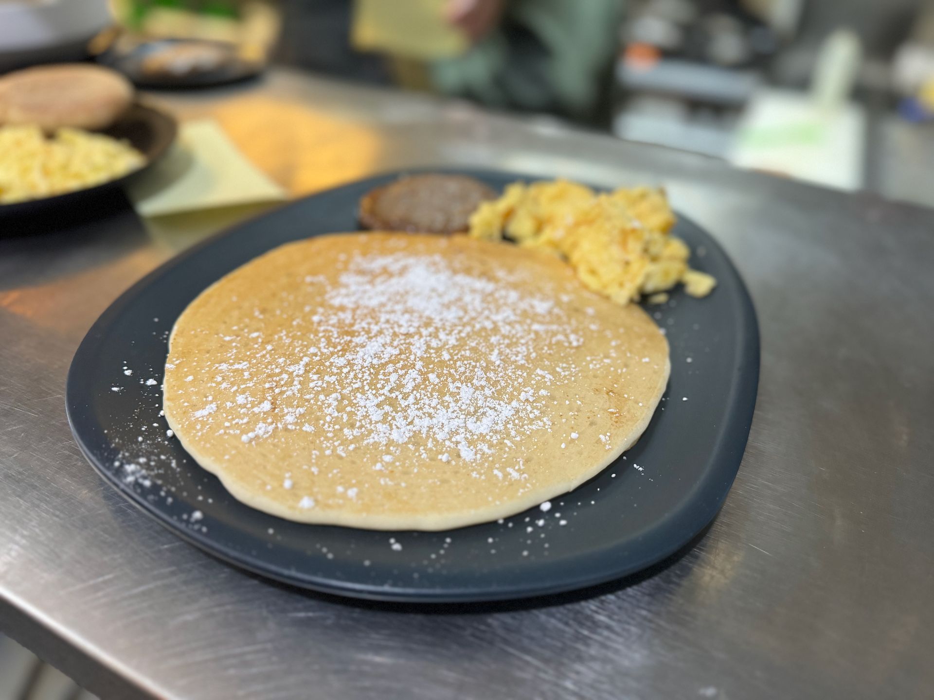 A pancake with powdered sugar and scrambled eggs on a black plate