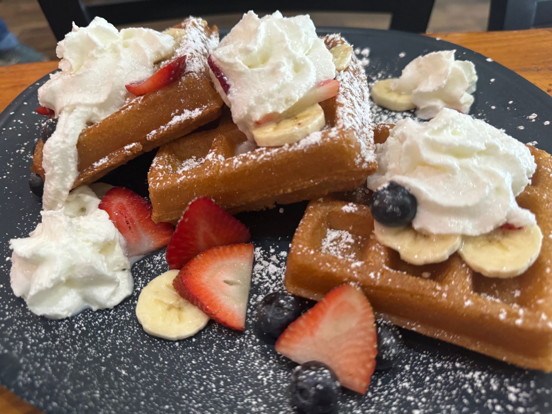 A plate of waffles with bananas strawberries and whipped cream