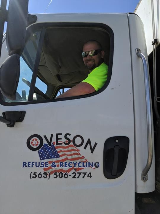 Man in a garbage truck, smiling. Truck says