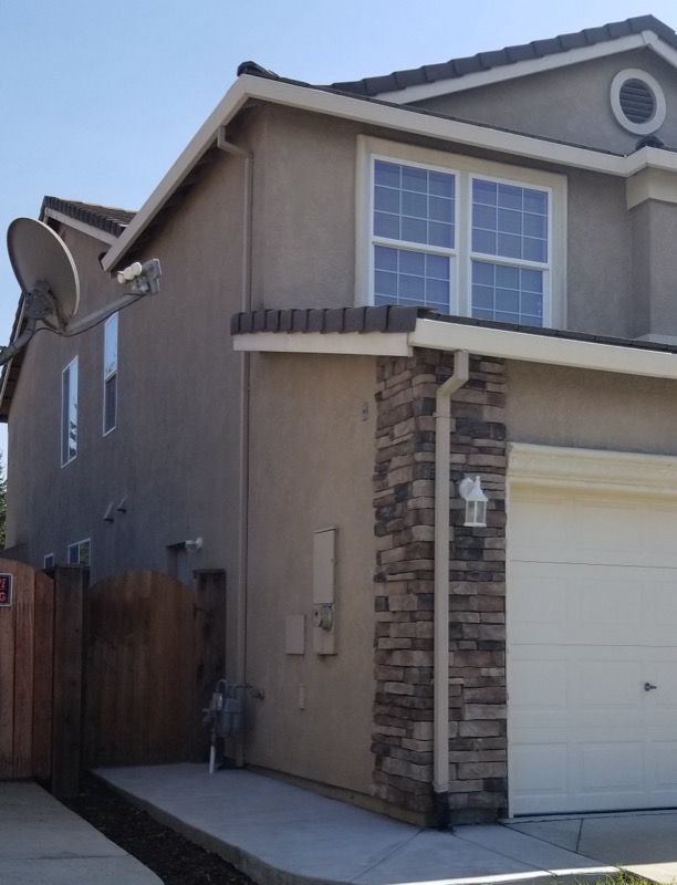 Two-story beige house exterior with white garage door and stone-trimmed corner detail