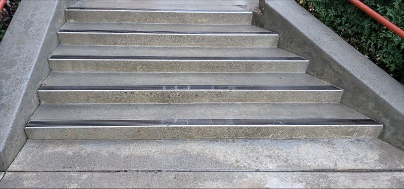 Concrete outdoor staircase with gray steps and a red handrail along the right side