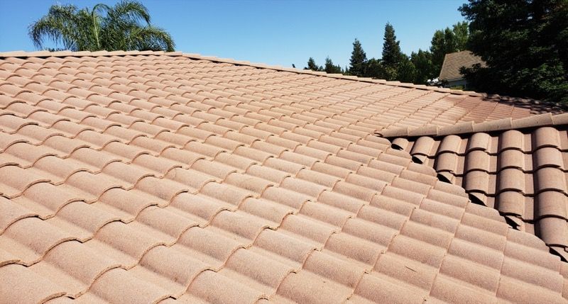 Terracotta tiled rooftop with a sloped valley and palm trees visible against a blue sky