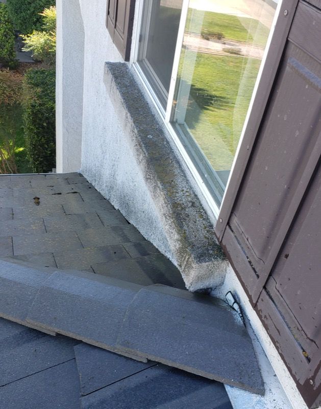 Damaged roof and wall beside a window, with a bent metal flashing piece resting on shingles
