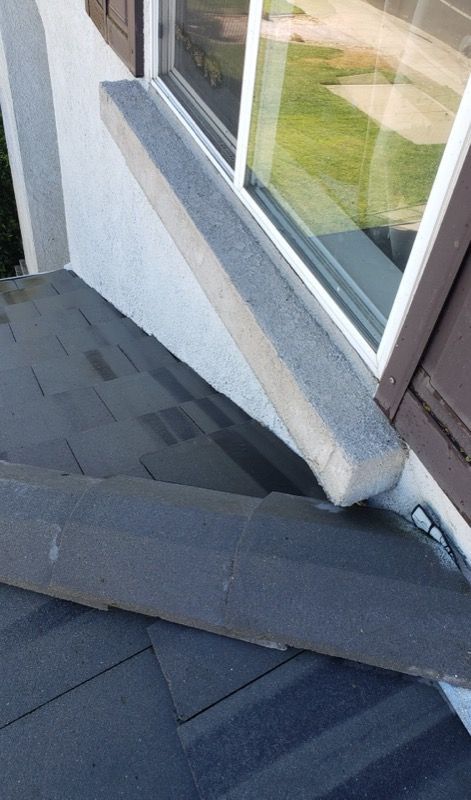 Roof shingles beside a window with a loose dark strip of roofing material